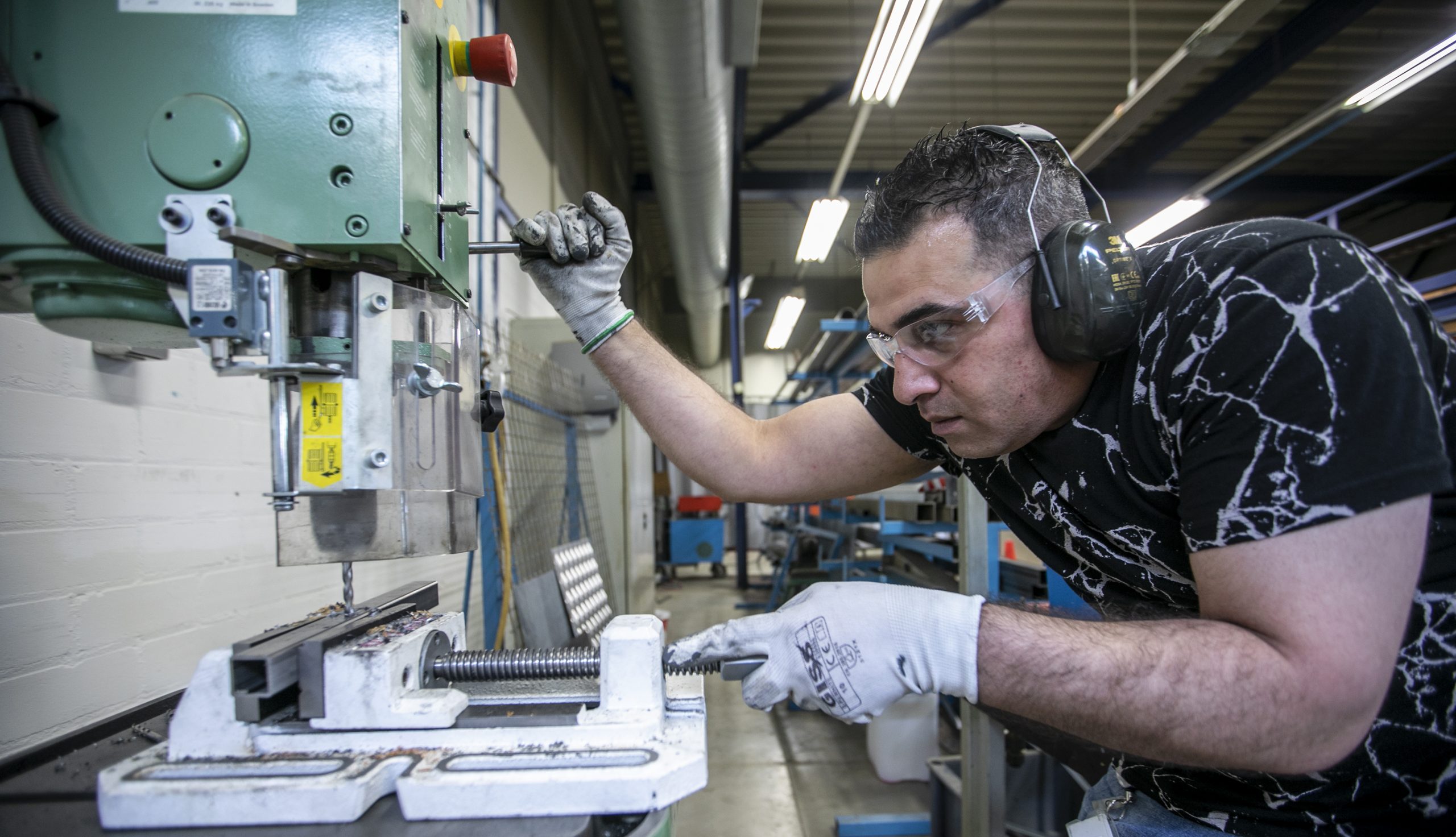 Een collega is bezig met boren. Hij draagt beschermingsmiddelen en kijkt geconcentreerd voor zich uit